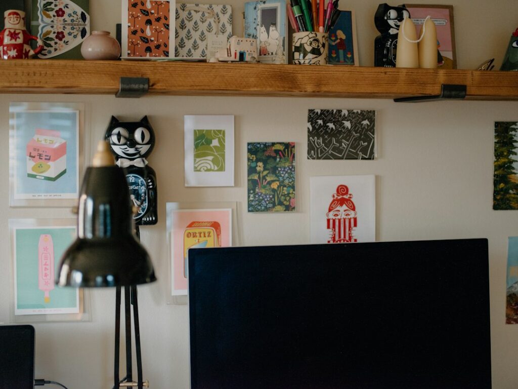 Framed artworks on a wall above a desk with a black lamp, a quiet workspace for writing emails to galleries