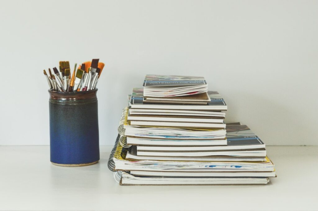A stack of blank art pads beside a jar of paintbrushes on a studio table, ready for writing an artist statement