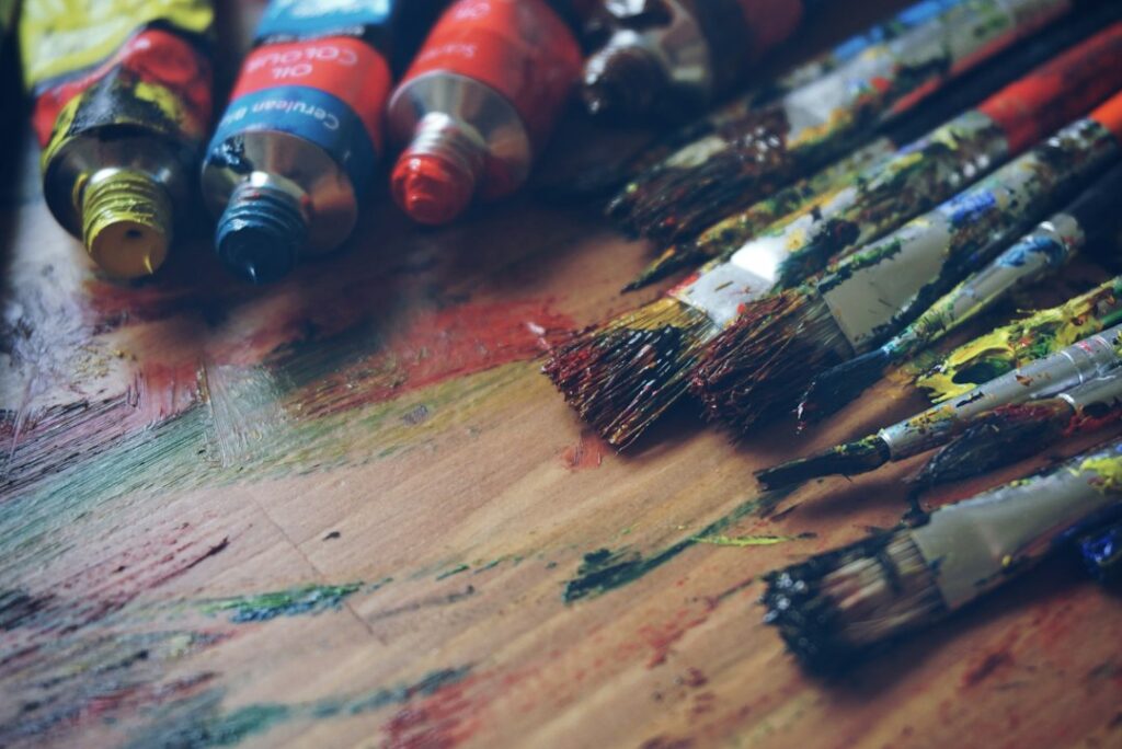 Well used paint brushes covered in colourful paint, resting on a table in an artist's studio