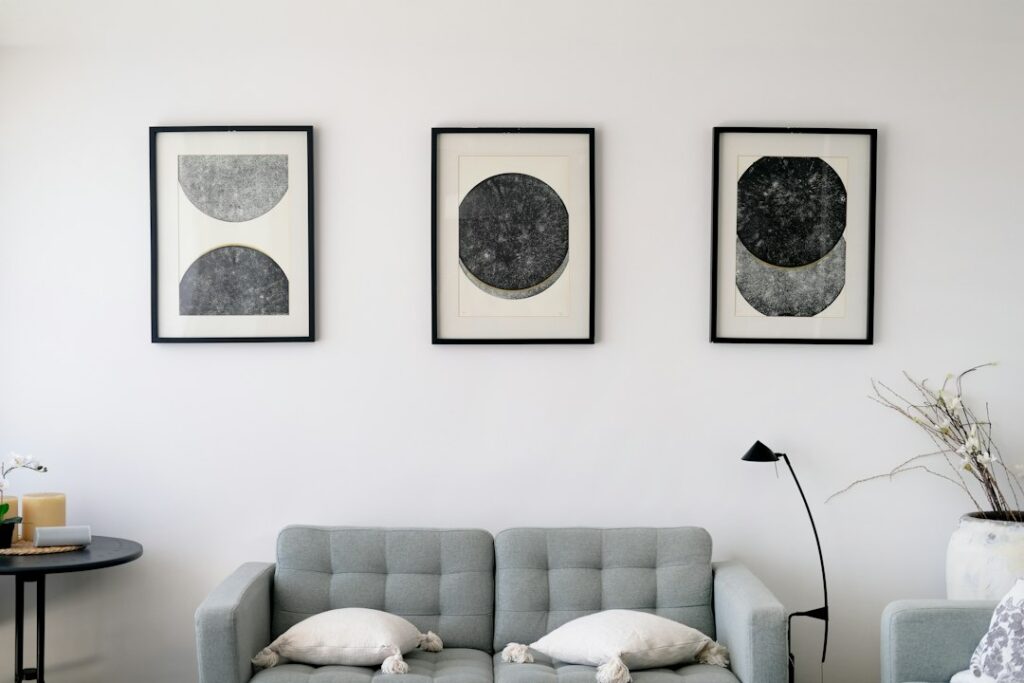 Three abstract paintings hanging on a living room wall above a grey sofa, showing how original art looks in a real home