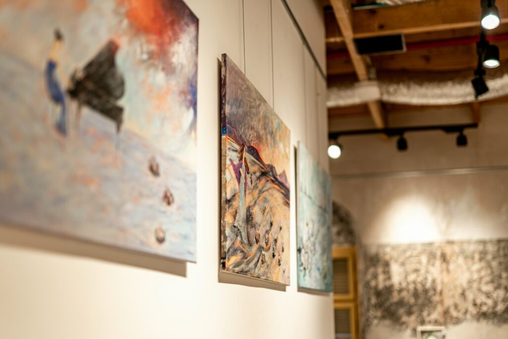 Expressive paintings hanging on a white gallery wall under warm spotlights
