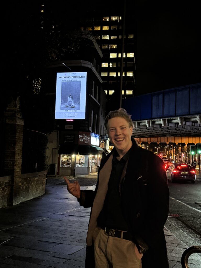 James Carter beside an Art on the Streets billboard at Waterloo, London, at night