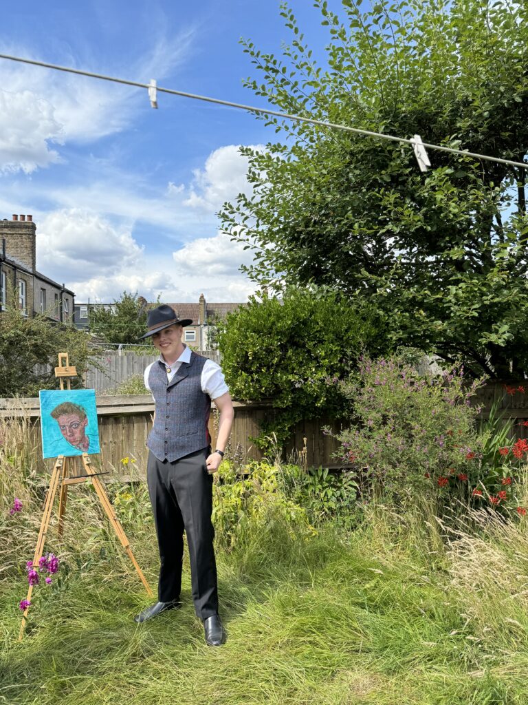 James Carter standing beside a painting on an easel in a garden