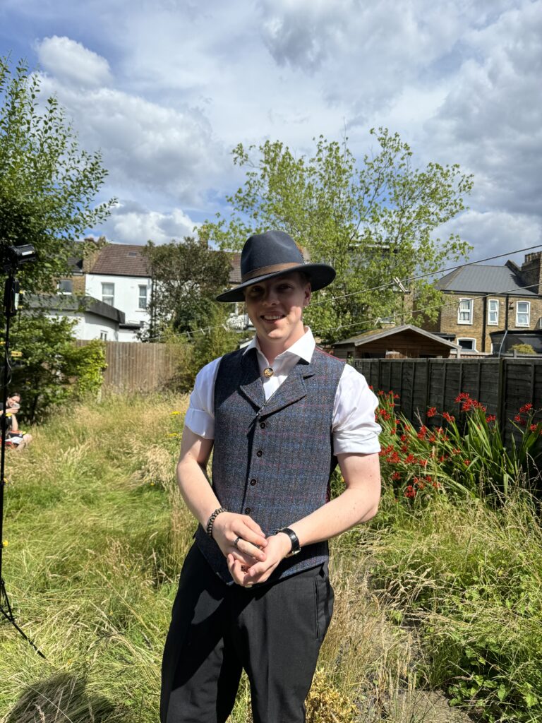 Portrait of James Carter in a fedora and waistcoat in a garden