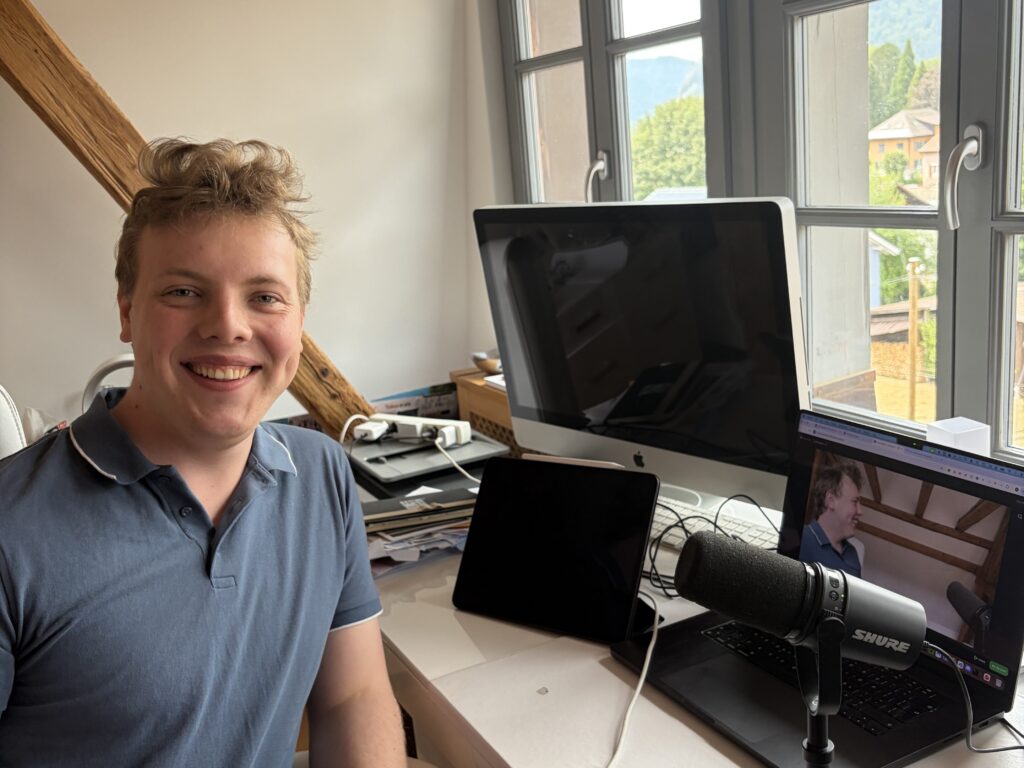 James Carter smiling at his desk with a microphone, laptop and monitor, set up for an online live session