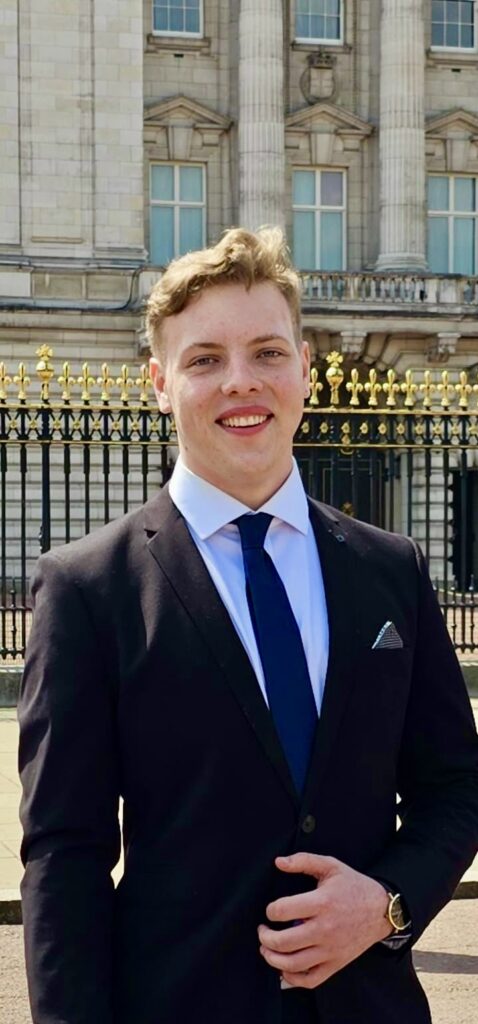 Portrait of James Carter in a suit at the gates of Buckingham Palace